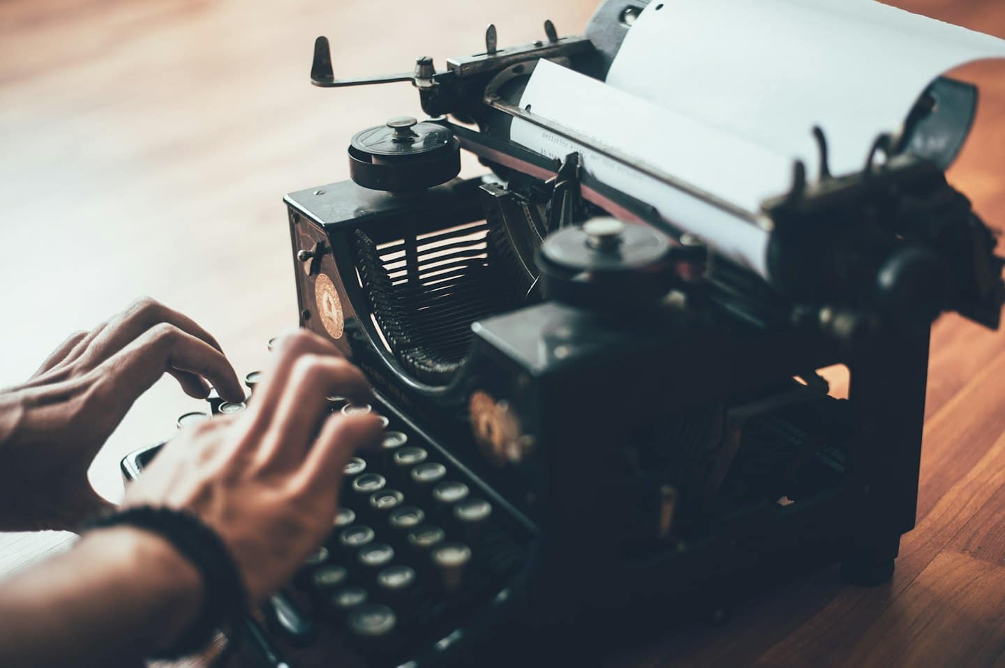 Mani che scrivono su una macchina da scrivere nera vintage su una scrivania di legno.