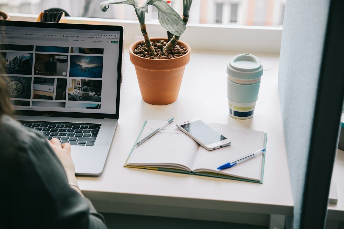 Persona che digita su un laptop a una scrivania con taccuino e tazza di caffè.