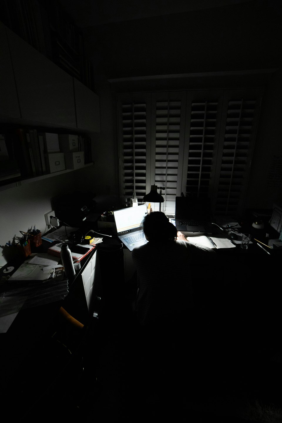 Persona che lavora al computer portatile su una scrivania disordinata in una stanza buia.